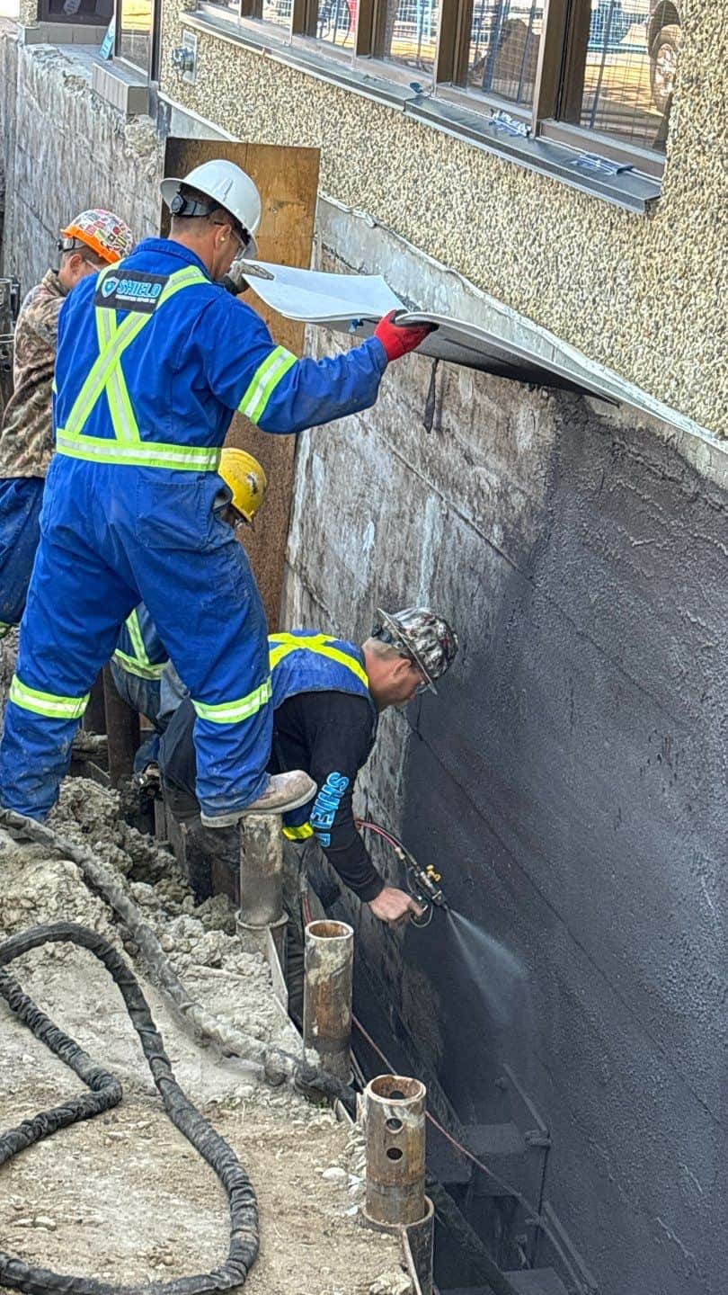 Image of Shield Foundation Repair employees spraying an application of WetSuit waterproofing product.