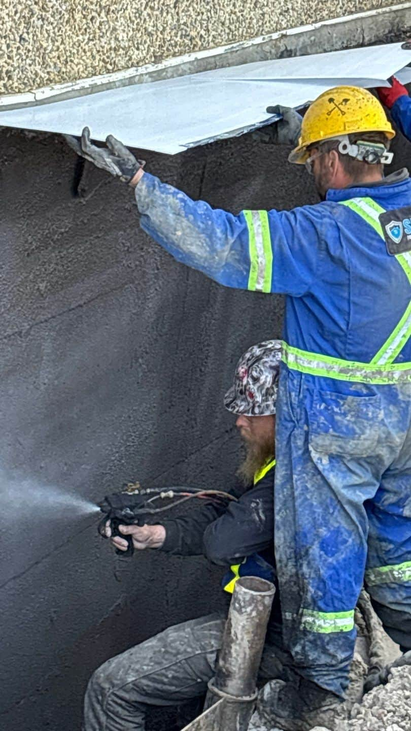 Image of Shield Foundation Repair employees spraying an application of WetSuit waterproofing product.